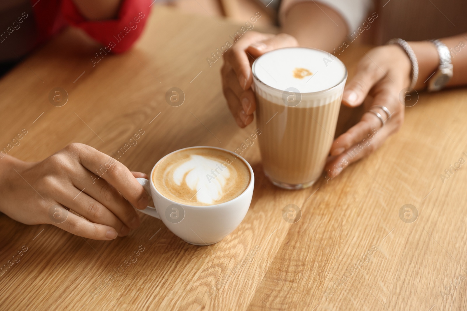 Photo of Women with cups of delicious coffee drinks at wooden table in cafe, closeup