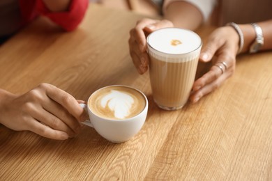 Photo of Women with cups of delicious coffee drinks at wooden table in cafe, closeup