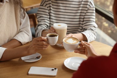 Women with cups of delicious coffee drinks at wooden table in cafe, closeup