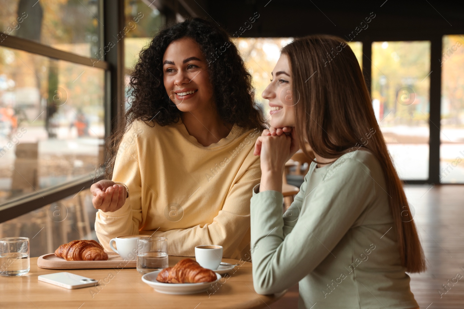 Photo of Happy women with coffee drinks chatting in cafe