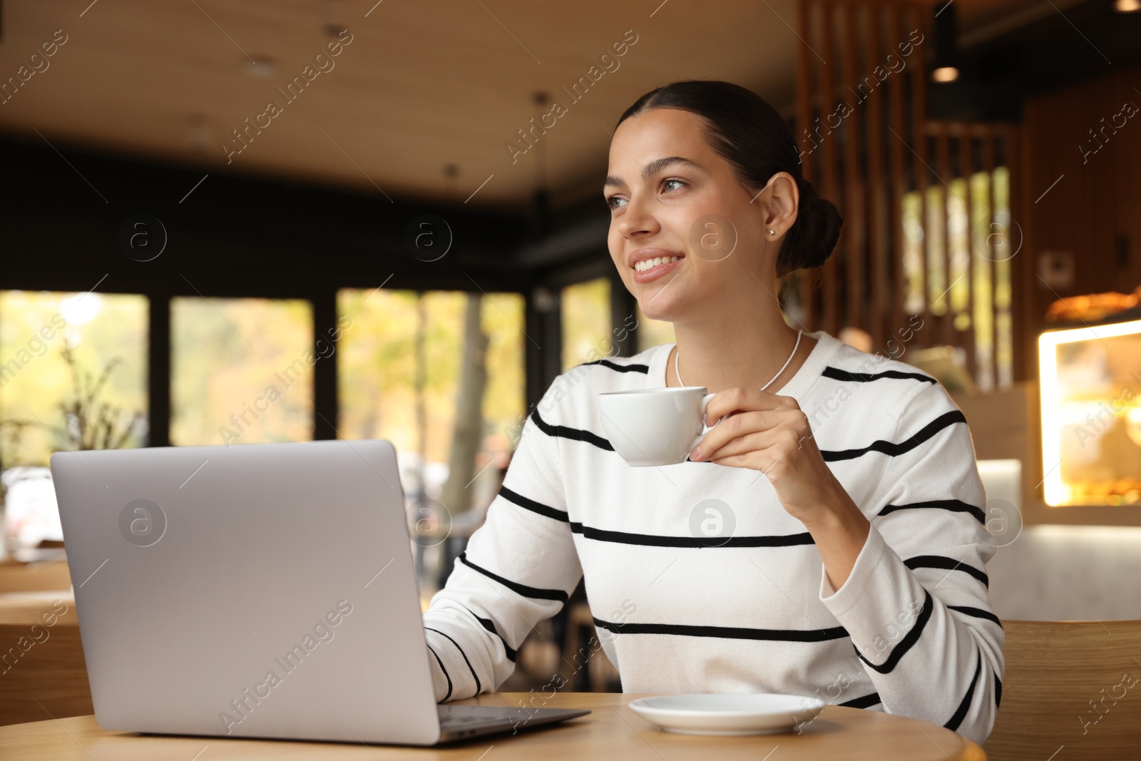 Photo of Woman with cup of coffee working on laptop in cafe