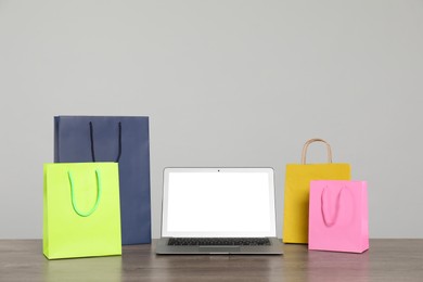 Photo of Internet shopping. Laptop and colorful paper bags on wooden table against grey background