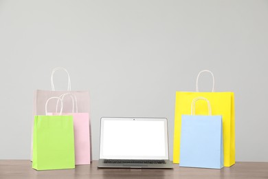 Photo of Internet shopping. Laptop and colorful paper bags on wooden table against grey background