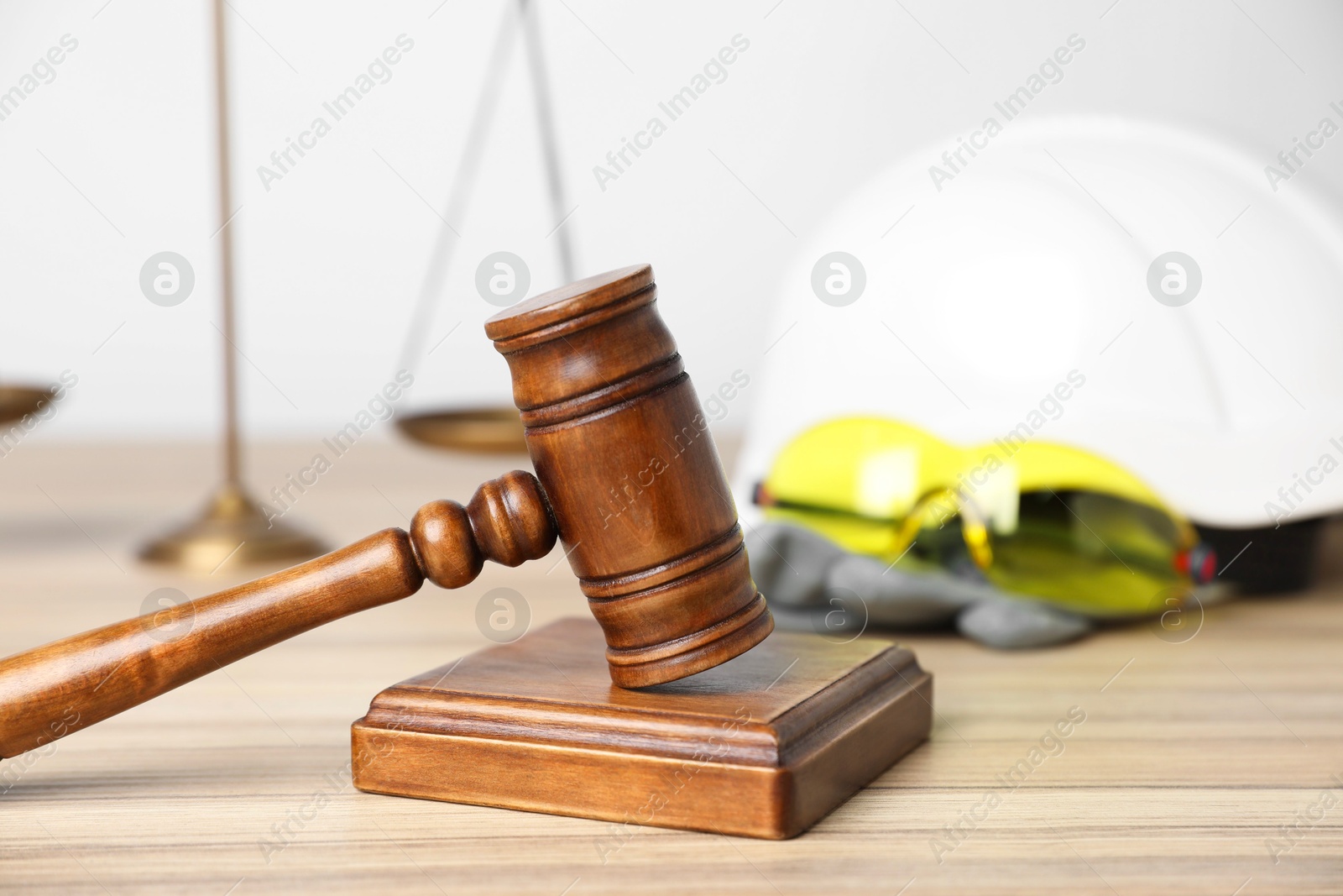 Photo of Accident at work concept. Gavel, scales and construction worker's protective gear on wooden table, selective focus