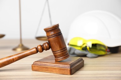 Photo of Accident at work concept. Gavel, scales and construction worker's protective gear on wooden table, selective focus