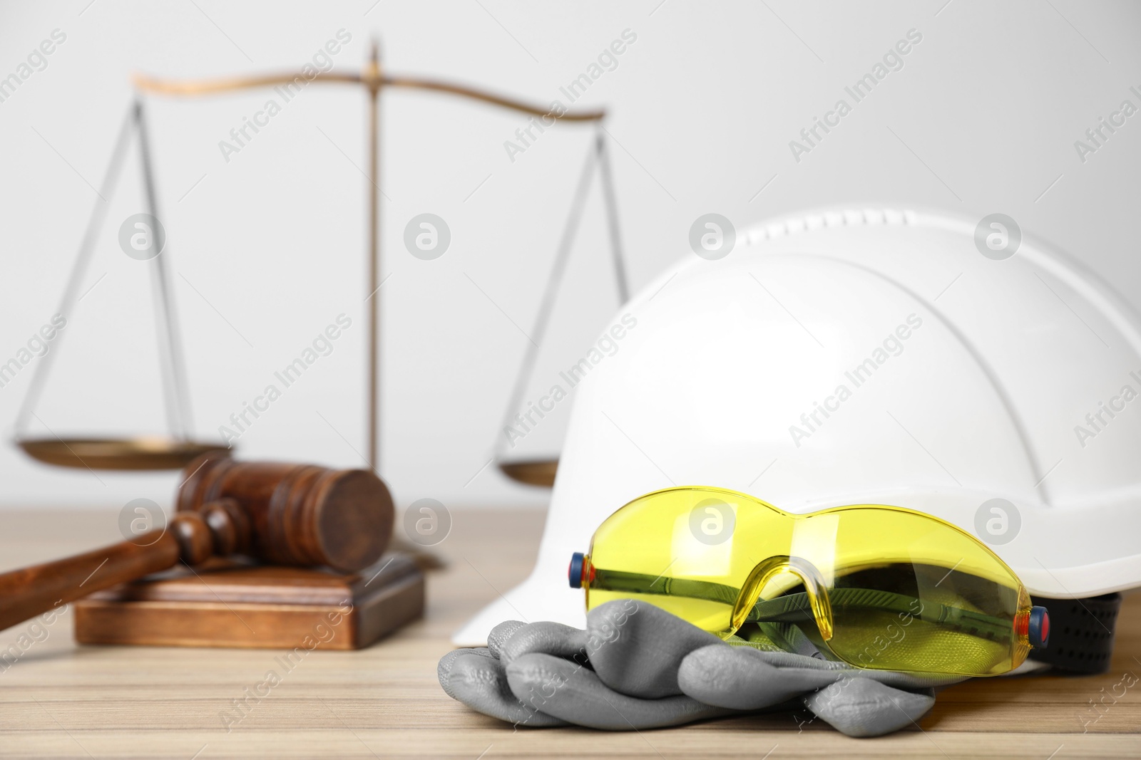 Photo of Accident at work concept. Gavel, scales and construction worker's protective gear on wooden table, selective focus