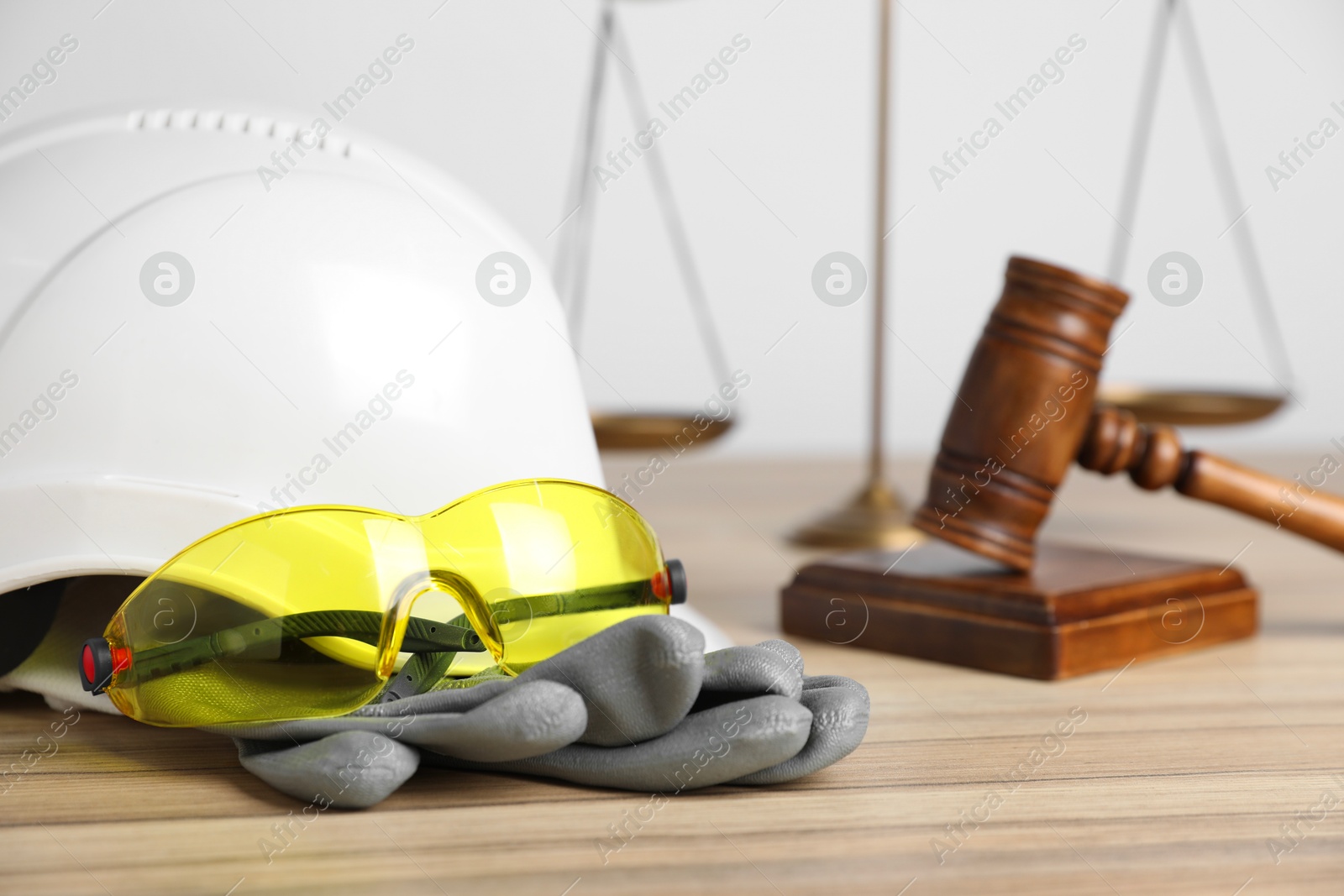 Photo of Accident at work concept. Gavel, scales and construction worker's protective gear on wooden table, selective focus