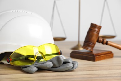 Photo of Accident at work concept. Gavel, scales and construction worker's protective gear on wooden table, selective focus