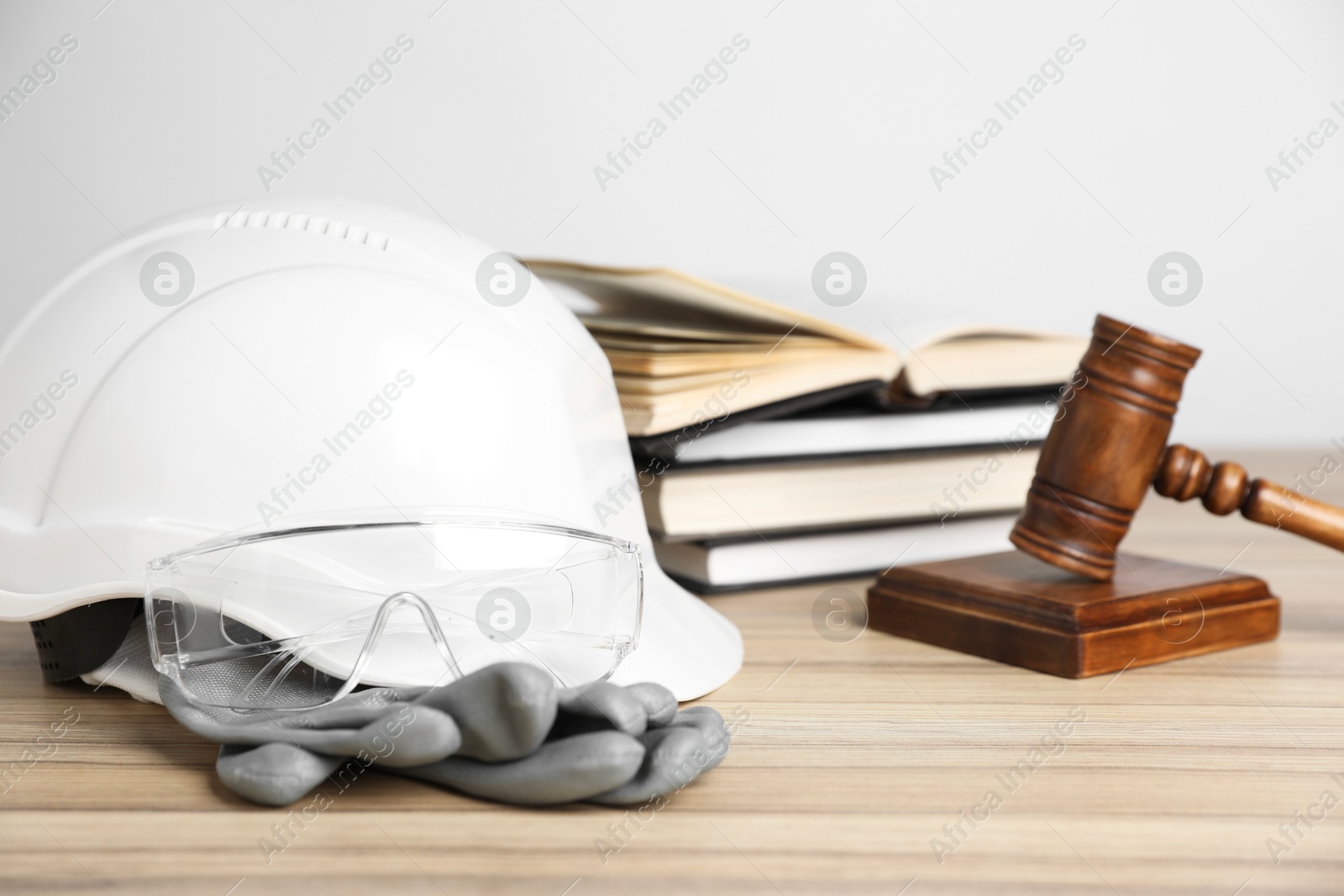 Photo of Accident at work concept. Gavel, books and construction worker's protective gear on wooden table, selective focus