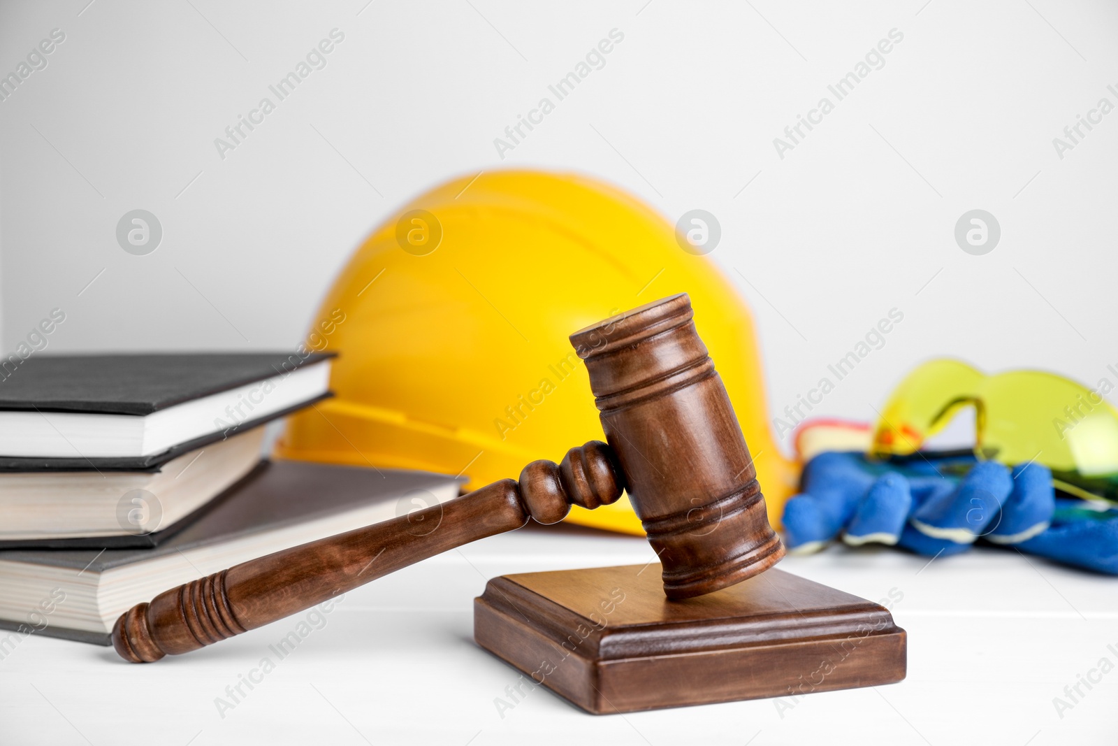 Photo of Accident at work concept. Gavel, books and construction worker's protective gear on white wooden table, selective focus