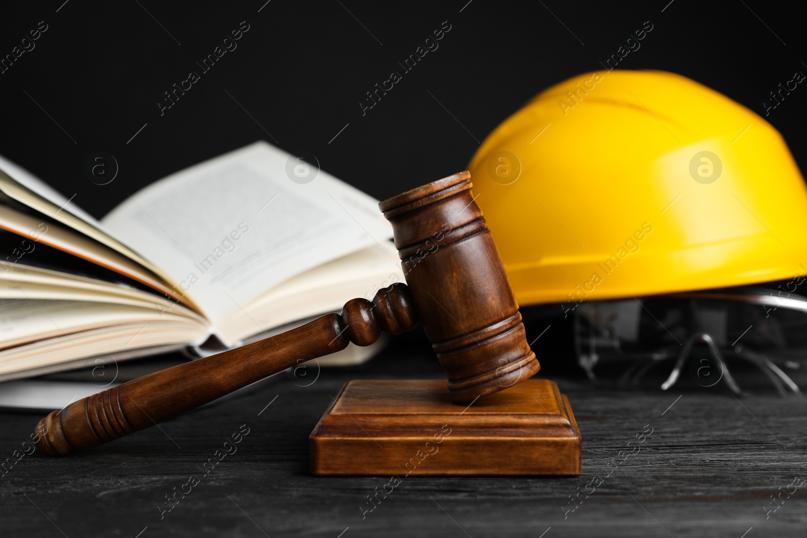 Photo of Accident at work concept. Gavel, book and construction worker's protective gear on black wooden table, selective focus