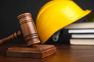 Photo of Accident at work concept. Gavel, books and construction worker's protective gear on wooden table, selective focus