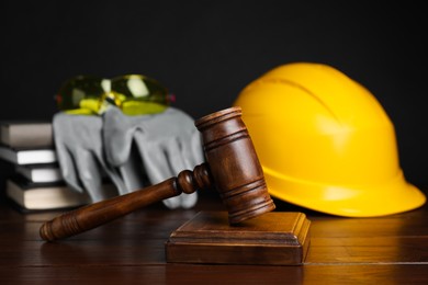 Photo of Accident at work concept. Gavel, books and construction worker's protective gear on wooden table, selective focus