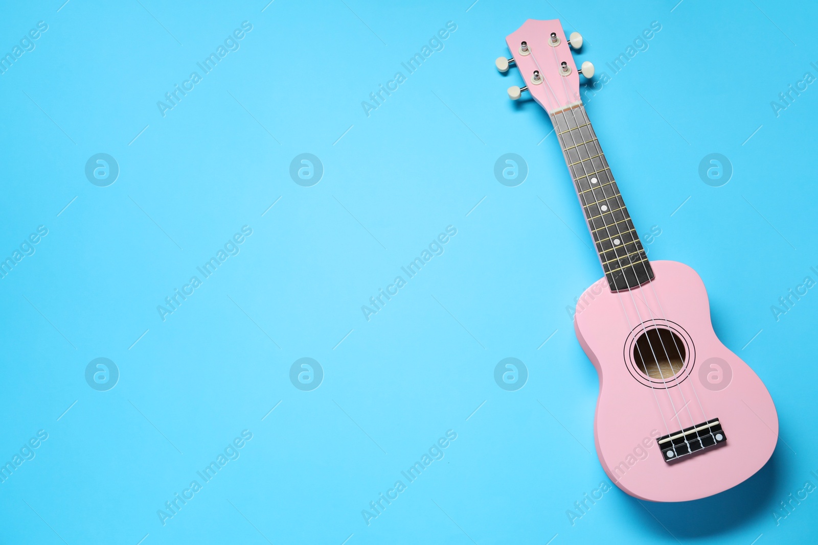 Photo of One ukulele on light blue background, top view. Space for text