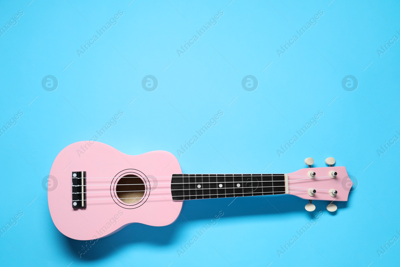 Photo of One ukulele on light blue background, top view. Space for text