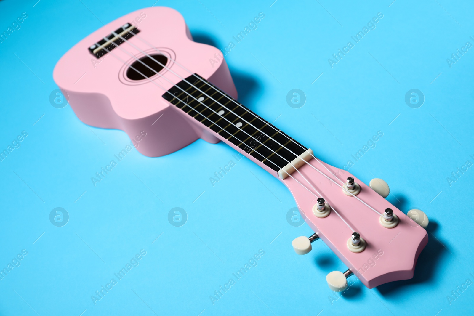 Photo of One ukulele on light blue background, closeup. String musical instrument