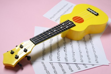 Photo of Ukulele and music sheets on pink background