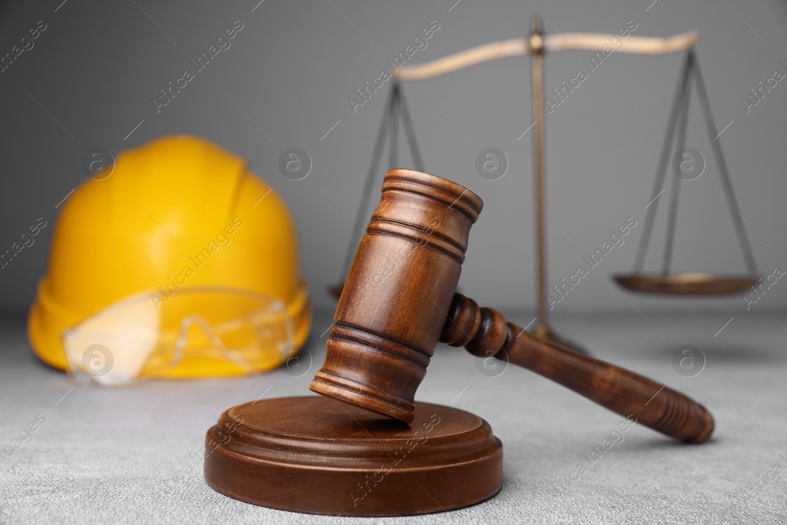 Photo of Accident at work. Gavel, safety equipment and scales on grey textured table, selective focus