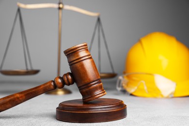 Photo of Accident at work. Gavel, safety equipment and scales on grey textured table, selective focus