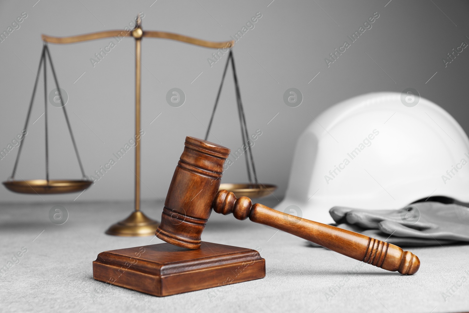 Photo of Accident at work. Gavel, safety equipment and scales on grey textured table