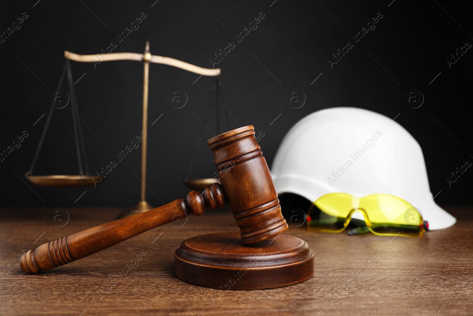 Photo of Accident at work. Gavel, safety equipment and scales on wooden table, selective focus