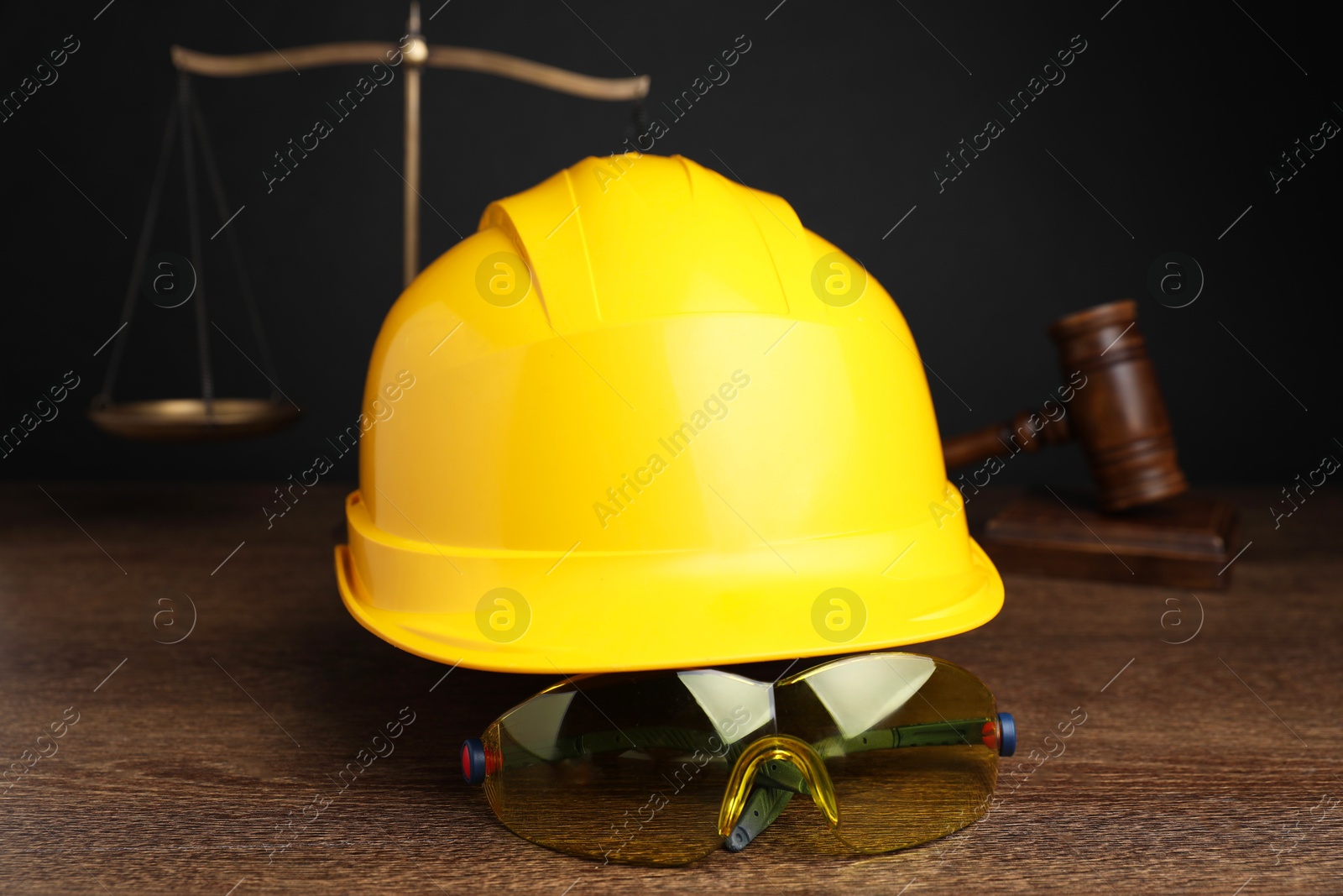 Photo of Accident at work. Hardhat, goggles, scales and gavel on wooden table, selective focus