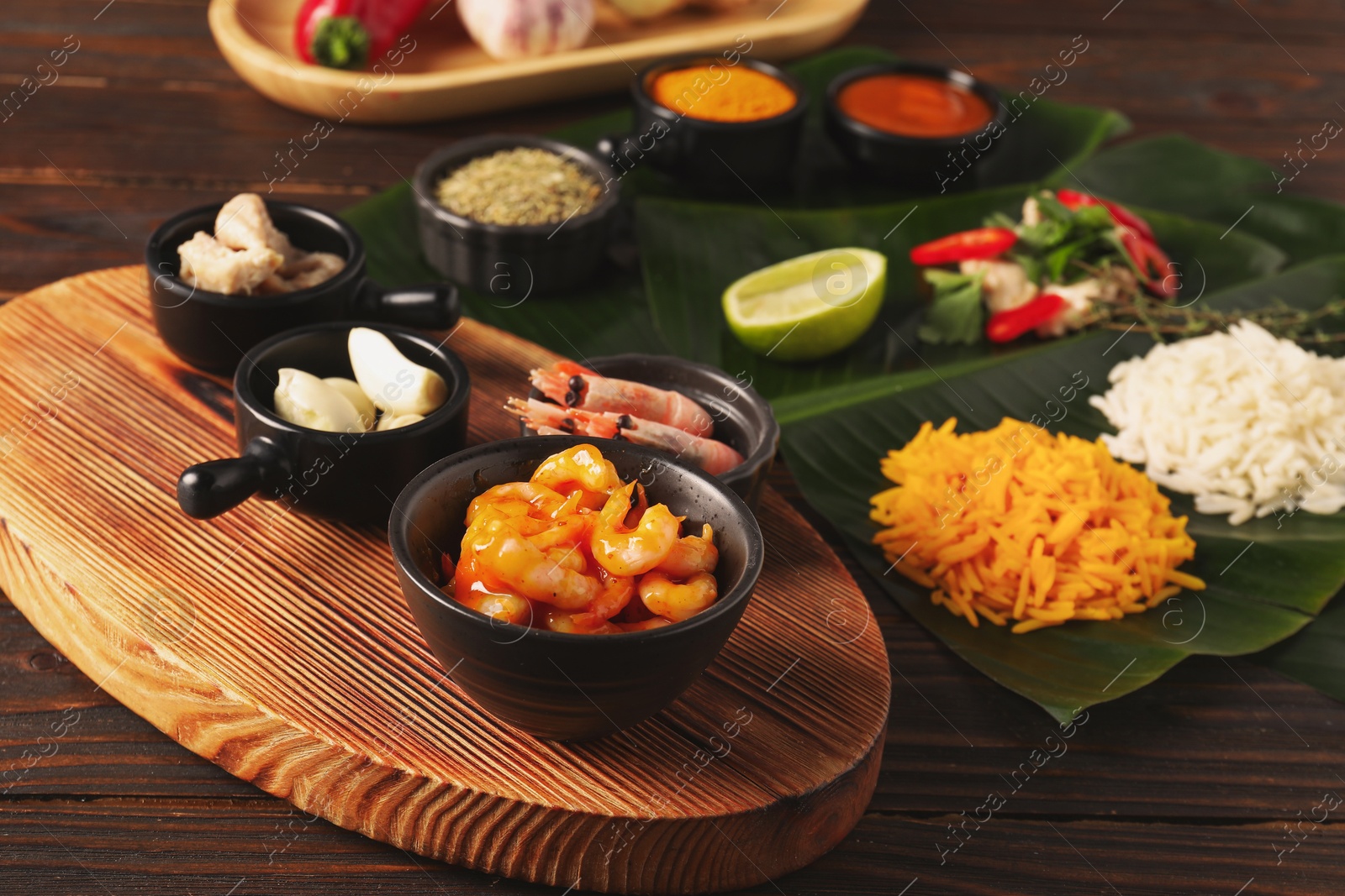 Photo of Cut banana leaves with different food, board, spices and sauce on wooden table, closeup