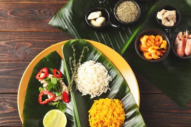 Cut banana leaves with different food and spices on wooden table, flat lay