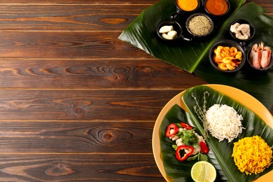 Cut banana leaves with different food, spices and sauce on wooden table, flat lay. Space for text