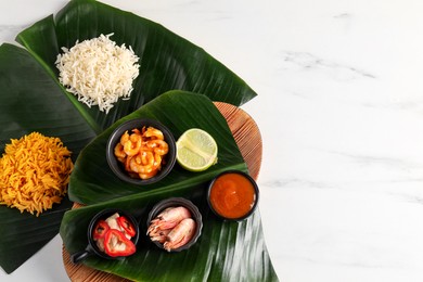 Photo of Cut banana leaves with different food and sauce on white marble table, flat lay. Space for text