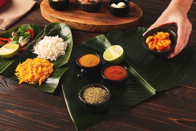 Woman setting table with cut banana leaves, different food, spices and sauce, closeup