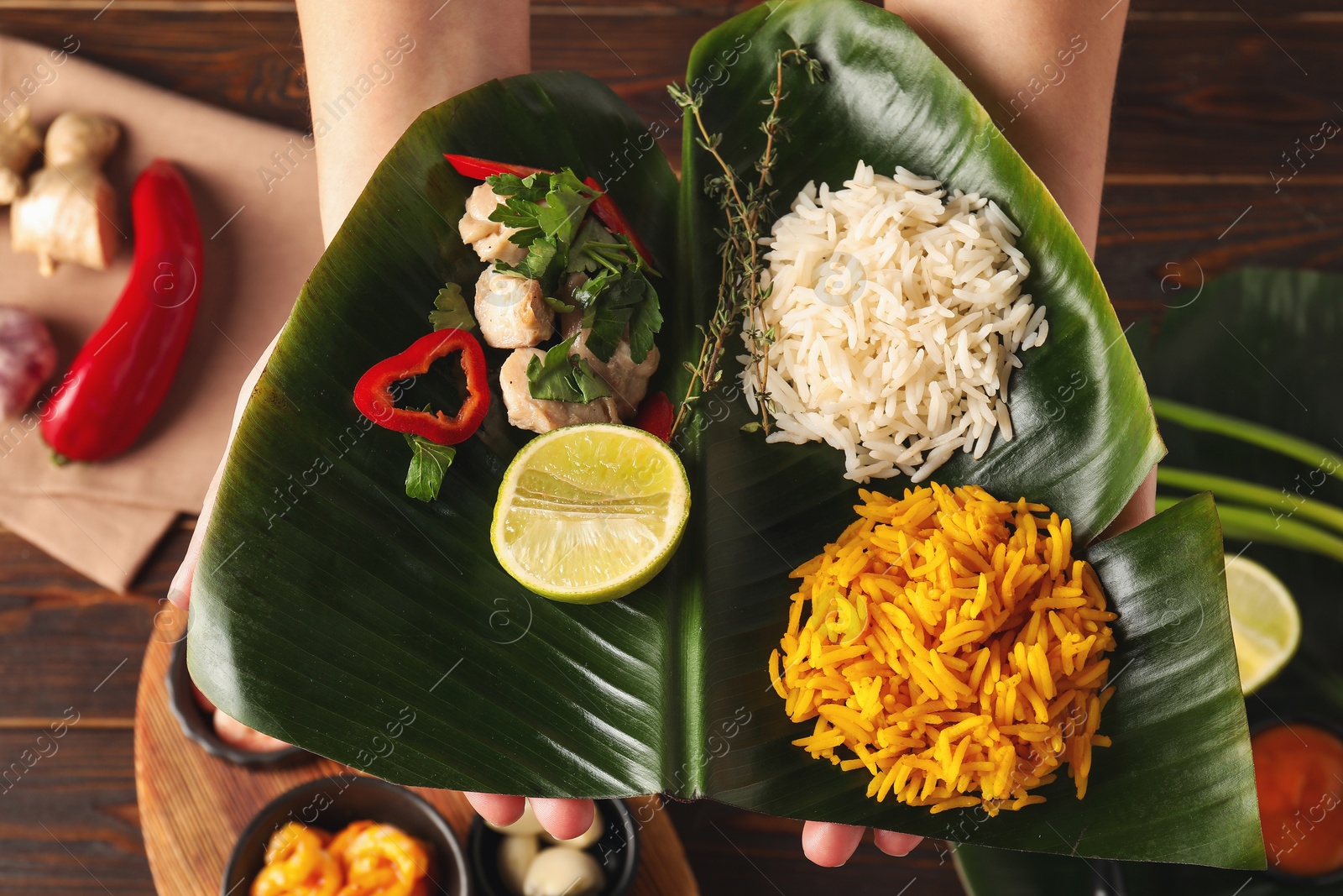 Photo of Woman holding cut banana leaf with different food at wooden table, top view