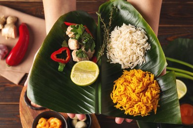 Woman holding cut banana leaf with different food at wooden table, top view