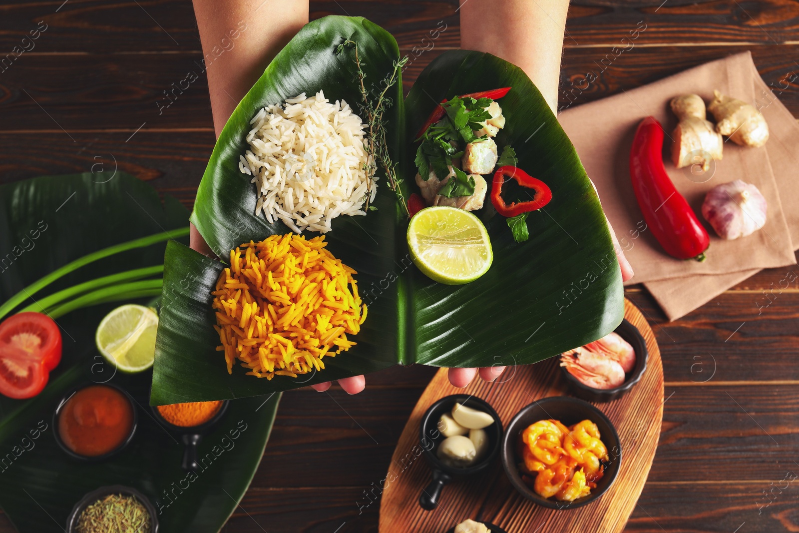 Photo of Woman holding cut banana leaf with different food at wooden table, top view