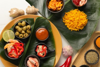 Cut banana leaves with different food, spices and sauce on white table, flat lay. Healthy eco serving