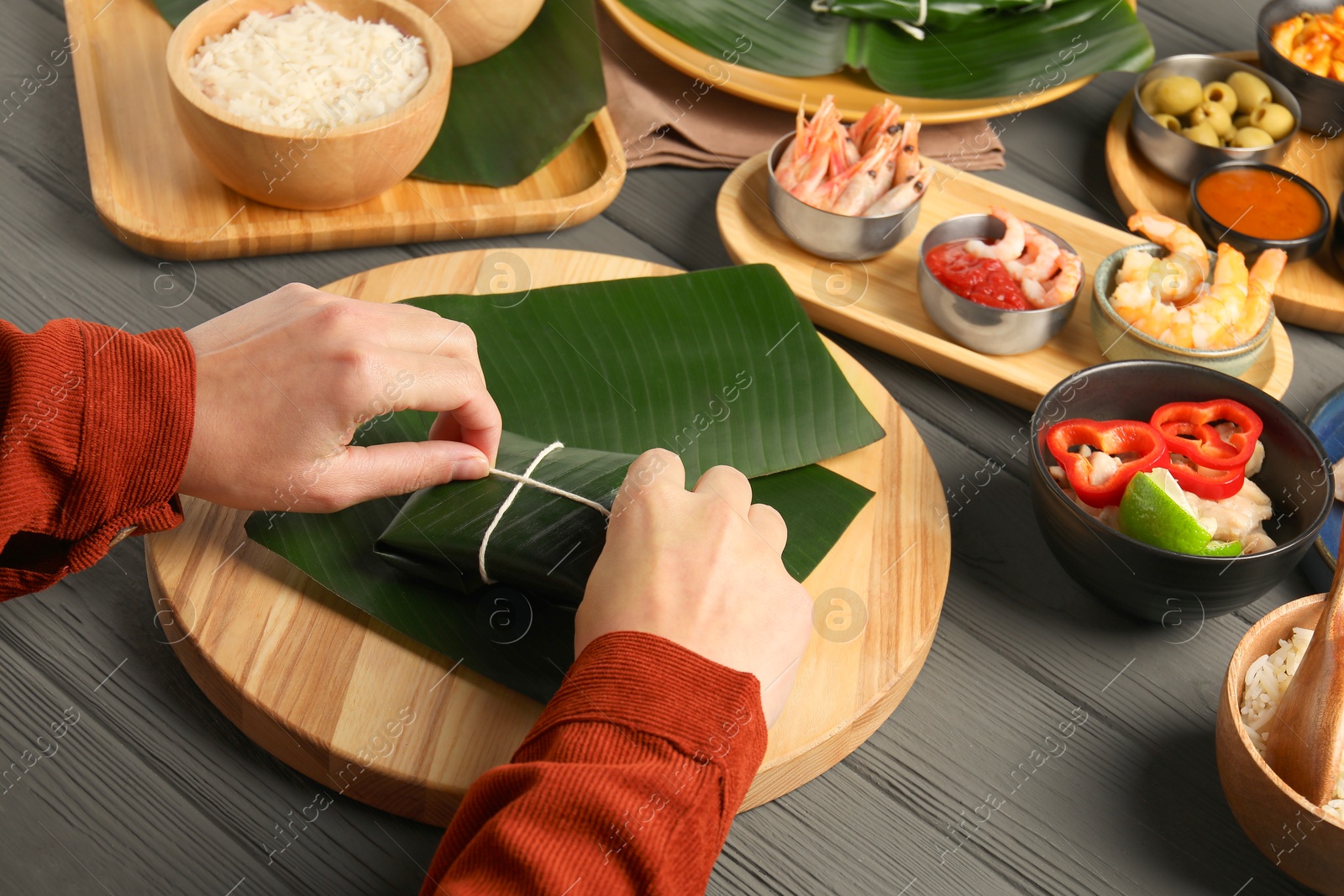 Photo of Woman tying banana leaf with food at wooden table with products, closeup. Healthy eco serving