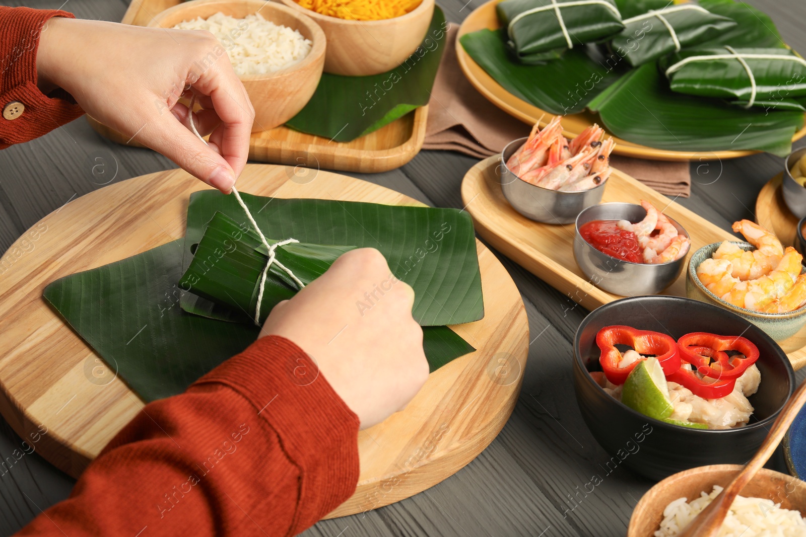 Photo of Woman tying banana leaf with food at wooden table with products, closeup. Healthy eco serving