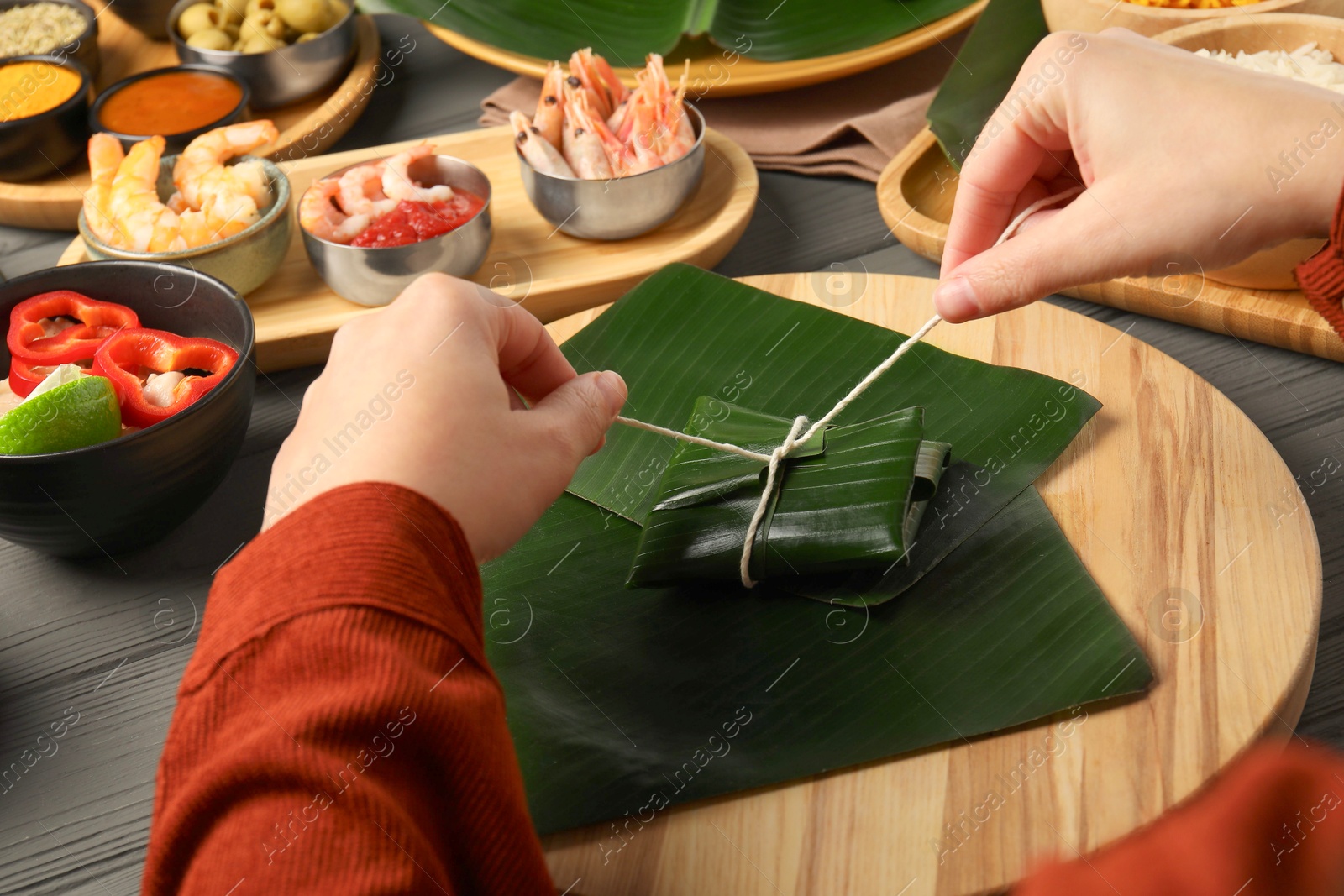 Photo of Woman tying banana leaf with food at wooden table with products, closeup. Healthy eco serving