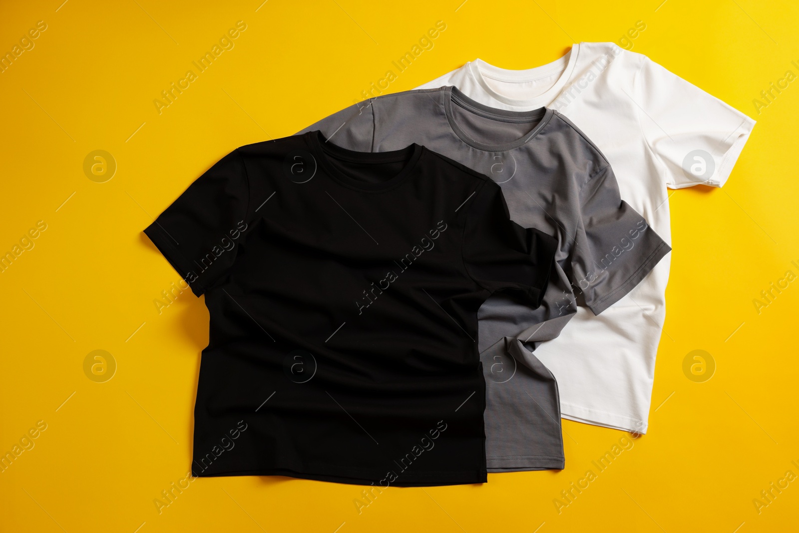 Photo of Blank t-shirts on yellow background, flat lay. Mockup for design