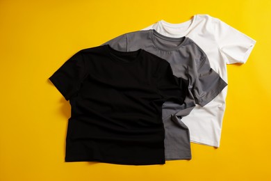 Photo of Blank t-shirts on yellow background, flat lay. Mockup for design