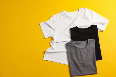 Photo of Blank t-shirts on yellow background, flat lay. Mockup for design