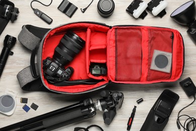 Photo of Professional photographer's equipment and backpack on light wooden background, flat lay