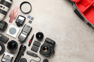 Photo of Professional photographer's equipment and backpack on light background, flat lay. Space for text