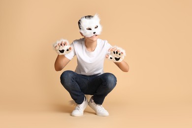 Photo of Quadrobics. Boy wearing cat mask and gloves on beige background