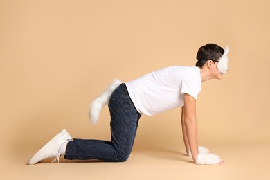 Photo of Quadrobics. Boy wearing cat mask, gloves and tail on beige background