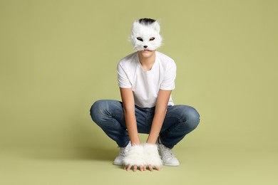 Photo of Quadrobics. Boy wearing cat mask and gloves on pale olive background