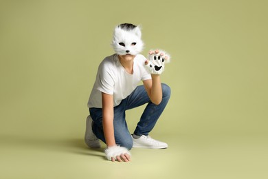 Photo of Quadrobics. Boy wearing cat mask and gloves on pale olive background