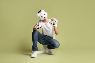 Photo of Quadrobics. Boy wearing cat mask, gloves and tail on pale olive background