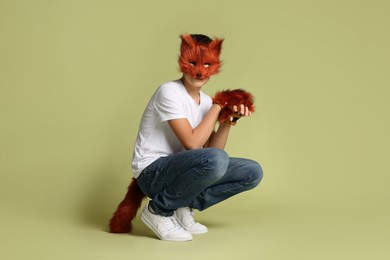 Photo of Quadrobics. Boy wearing fox mask, gloves and tail on pale olive background