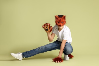 Photo of Quadrobics. Boy wearing fox mask, gloves and tail on pale olive background